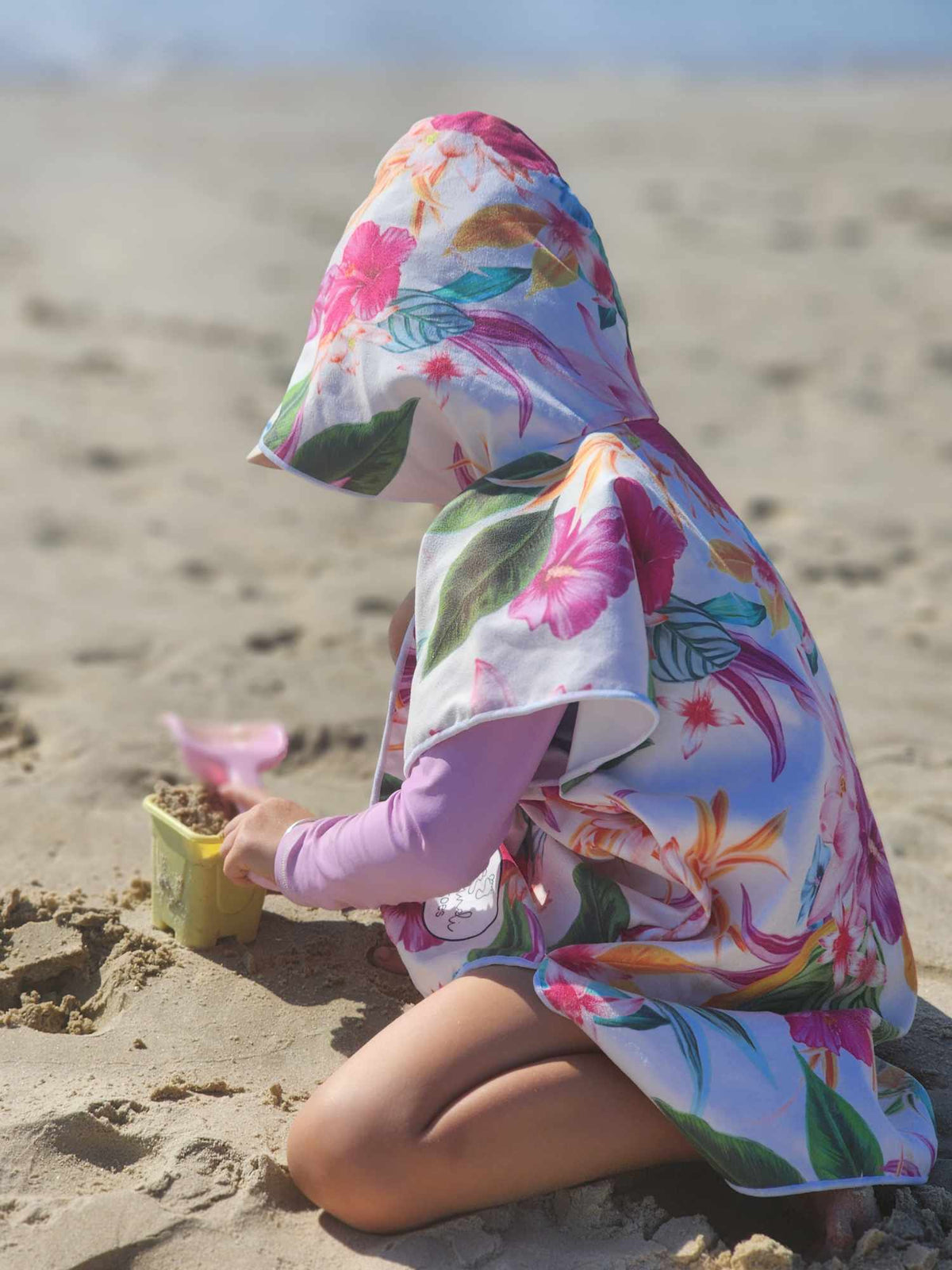 Playing with her sand toys this young girl is wearing her sand free hooded towel on the beach