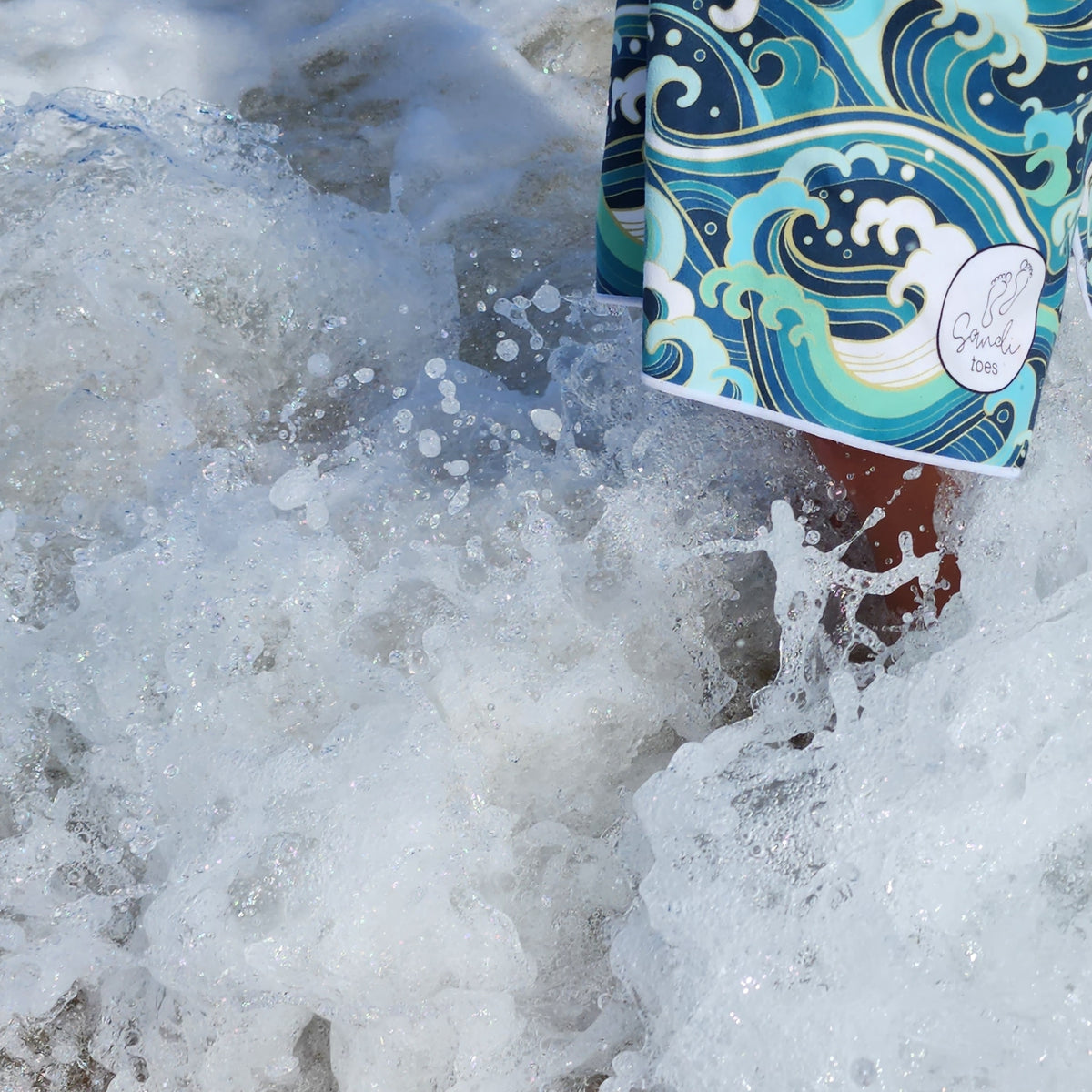 Wading in the beach waves is a boy with a wipeout showing the sandi toes logo