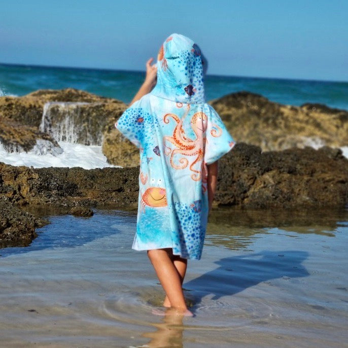 Here is a boy wearing Under the Sea sand free hoodie towel at Currumbin Beach Queensland wading in the water next to rocks